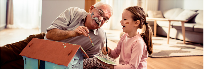 A little girl colouring a dollhouse with her grandfather